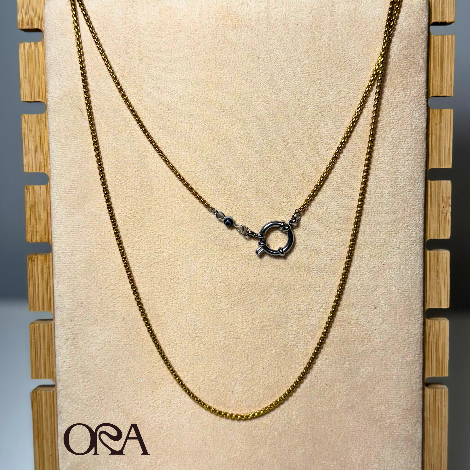 Gold Box Chain Necklace with silver clasp 
on a display board with 'ORA' branding
