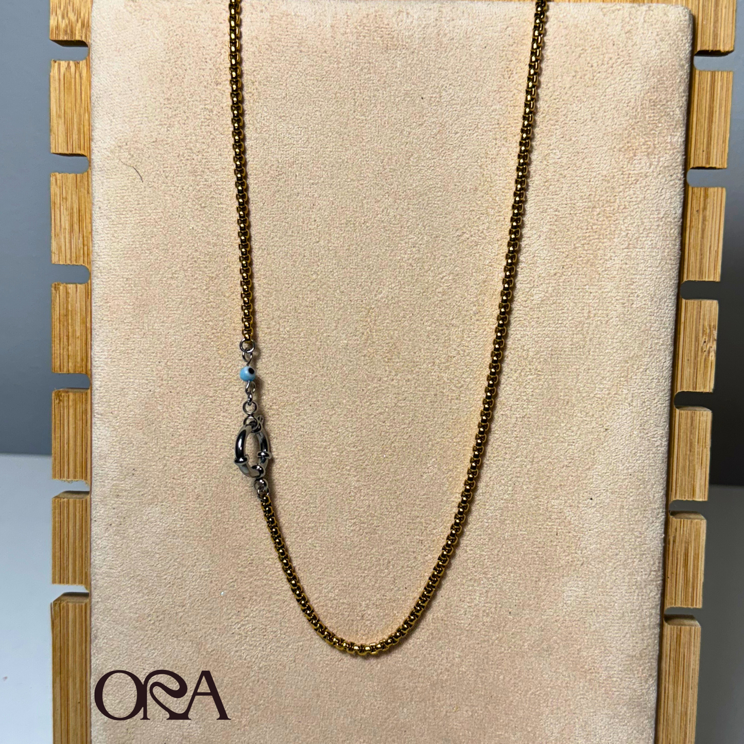 Box chain Necklace in gold with silver clasp on a beige board with 'ORA' branding